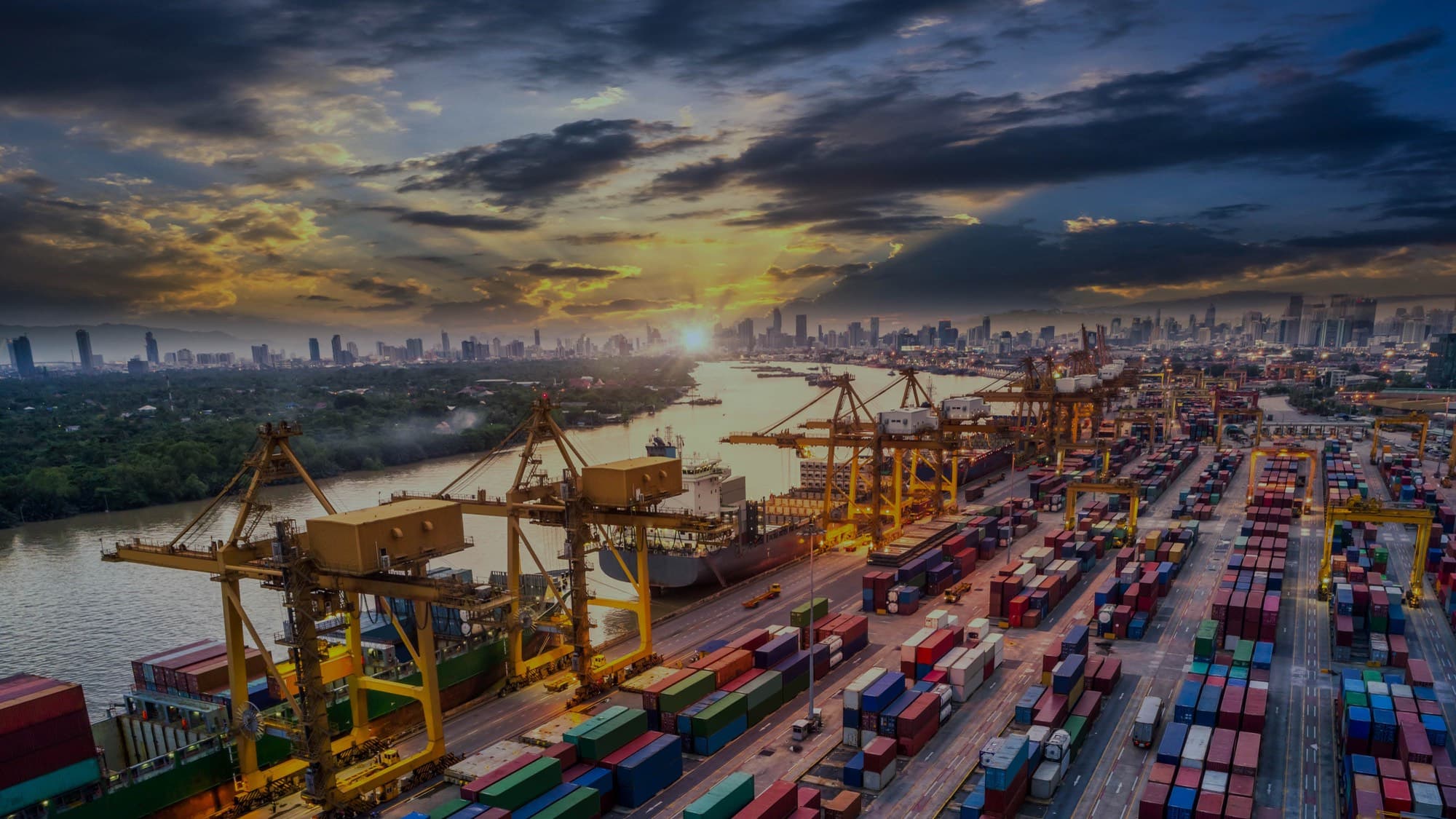 A container port at sunset, cranes loading a ship beside stacked containers
